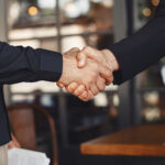Close-up of two people in dark suits shaking hands in a café