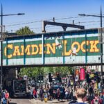 Crowds on Camden High Street beneath the iconic Camden Lock railway bridge in London on a sunny day