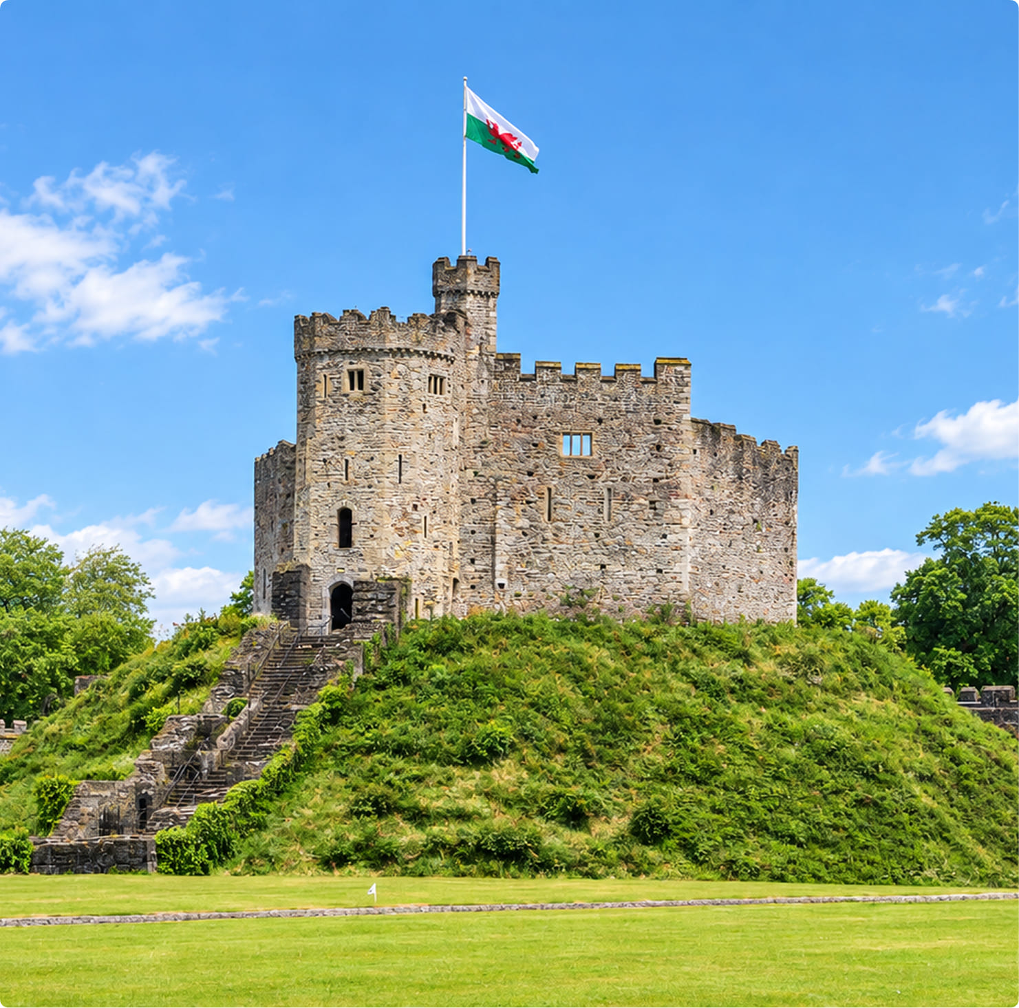 Norman keep of Cardiff Castle on a grassy mound with the Welsh flag flying above on a sunny day