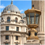 Ornate brass street lamp bearing the City of London crest in front of a domed historic building with a clock