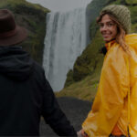 Couple holding hands in front of waterfall, the woman in a yellow rain poncho smiling back at the camera