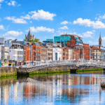 The Ha'penny Bridge over the River Liffey in Dublin, with colourful quayside buildings reflected in the water on a sunny day
