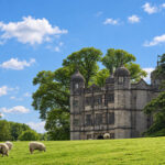 Sheep grazing on a sunny lawn in front of an Elizabethan stone manor house with domed corner turrets