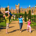 Father lifting his son while mother and daughter walk hand in hand through the gardens of an English country house