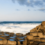 Athlete striking a discus-throwing pose on top of the hexagonal basalt columns of the Giant's Causeway, with waves crashing behind