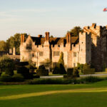 Rider on a grey horse crossing the lawn in front of Hever Castle and its topiary gardens in Kent, in warm evening light
