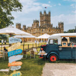 Vintage van refreshment stall and hand-painted drinks signpost on the lawn in front of Highclere Castle in Hampshire
