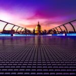 Millennium Bridge in London leading to an illuminated St Paul's Cathedral under a purple sunset sky
