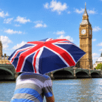 Tourist holding a Union Jack umbrella beside the River Thames, looking toward Big Ben, Westminster Bridge and the Houses of Parliament
