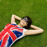 Smiling woman in sunglasses and a Union Jack t-shirt relaxing on the grass with her hands behind her head